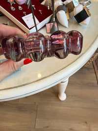 A hand with red nail polish holds a translucent purple glass hair claw clip in front of a white table inside a jewelry store.