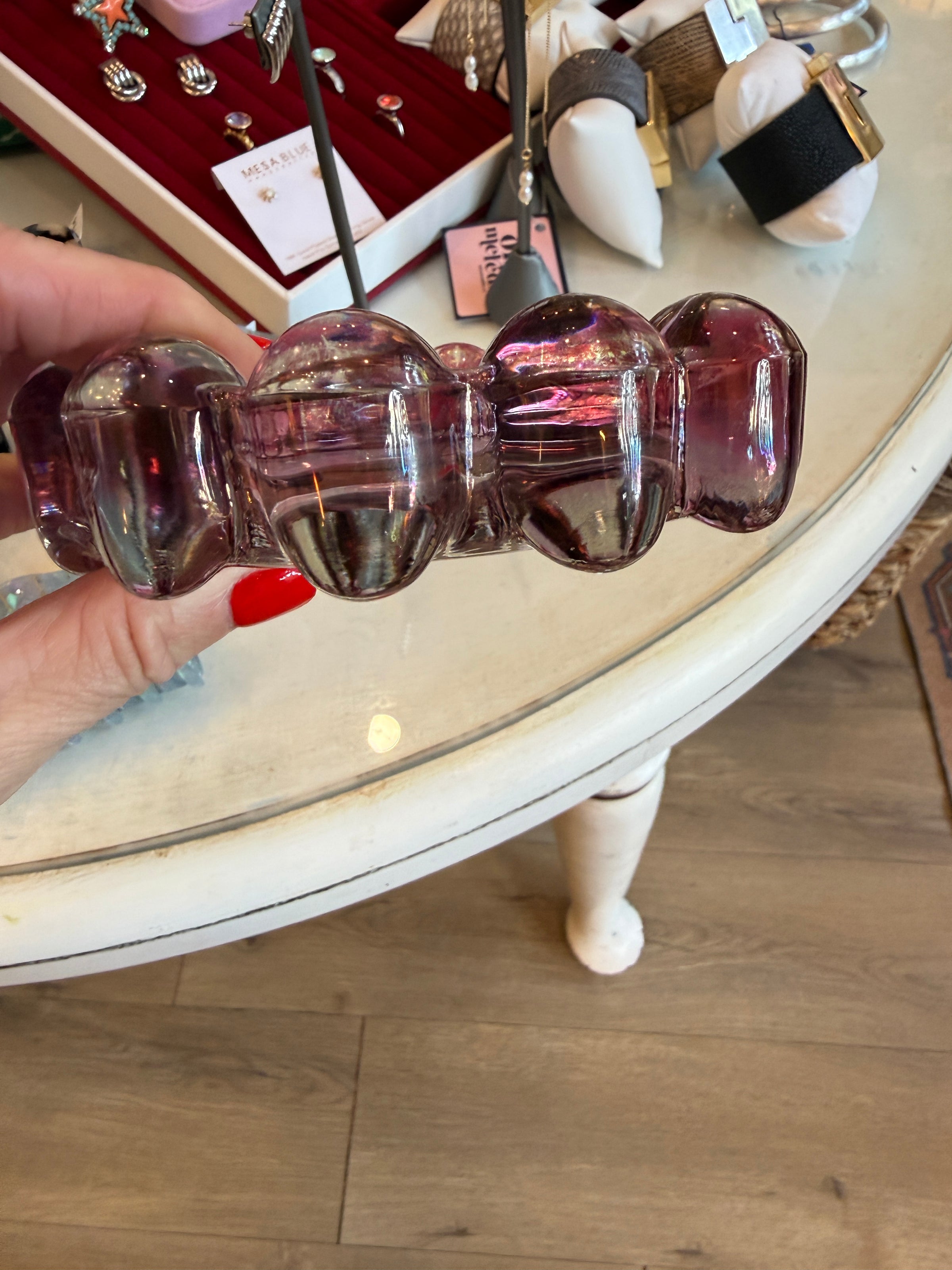 A hand with red nail polish holds a translucent purple glass hair claw clip in front of a white table inside a jewelry store.