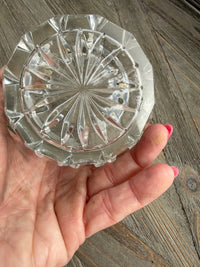 Hand holding a clear crystal dish with intricate design on a wooden surface