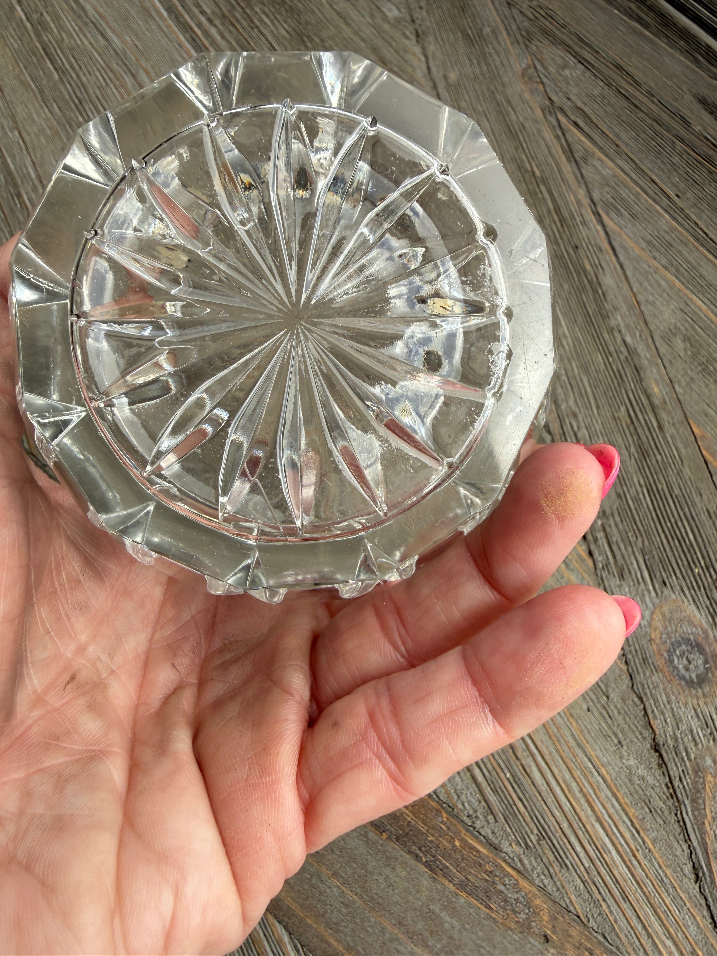Hand holding a clear crystal dish with intricate design on a wooden surface