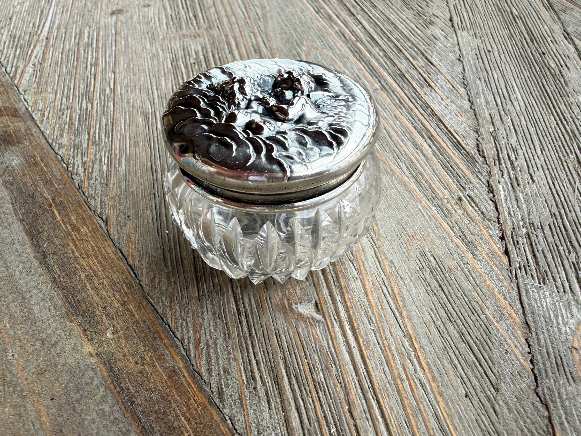 Decorative glass container with silver lid on a wooden surface