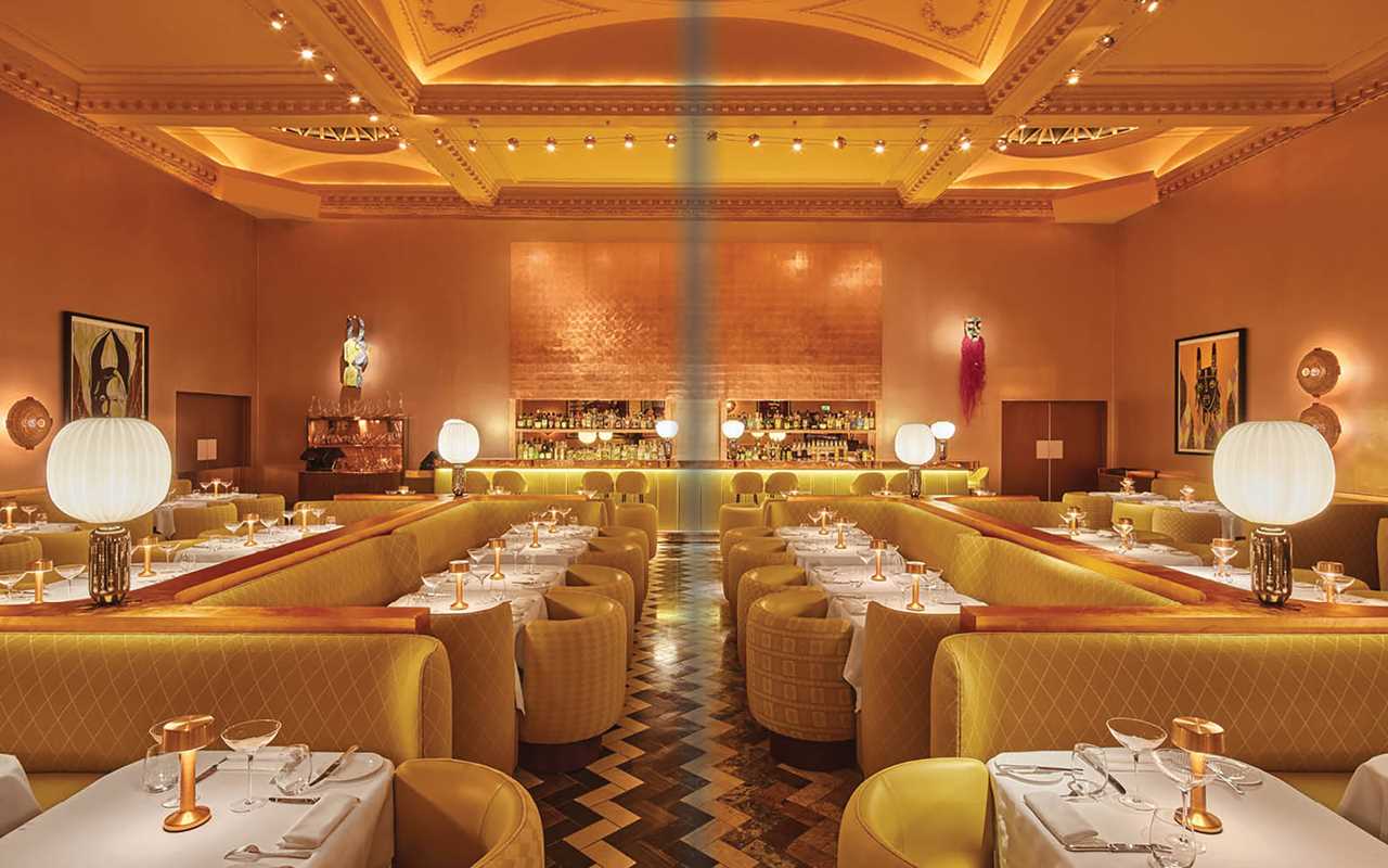 Luxurious restaurant interior with yellow chairs and tables, dim lighting, and decorative elements.