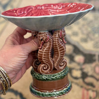 Decorative ceramic bowl with seahorse design held by a hand on a patterned rug.