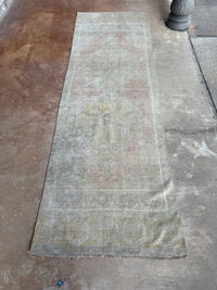 A long, distressed runner rug with faded beige, gray, and muted red tones, laid out on a concrete floor.