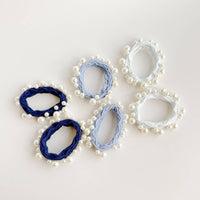 Set of pearl-embellished hair scrunchies in blue and white on a light background