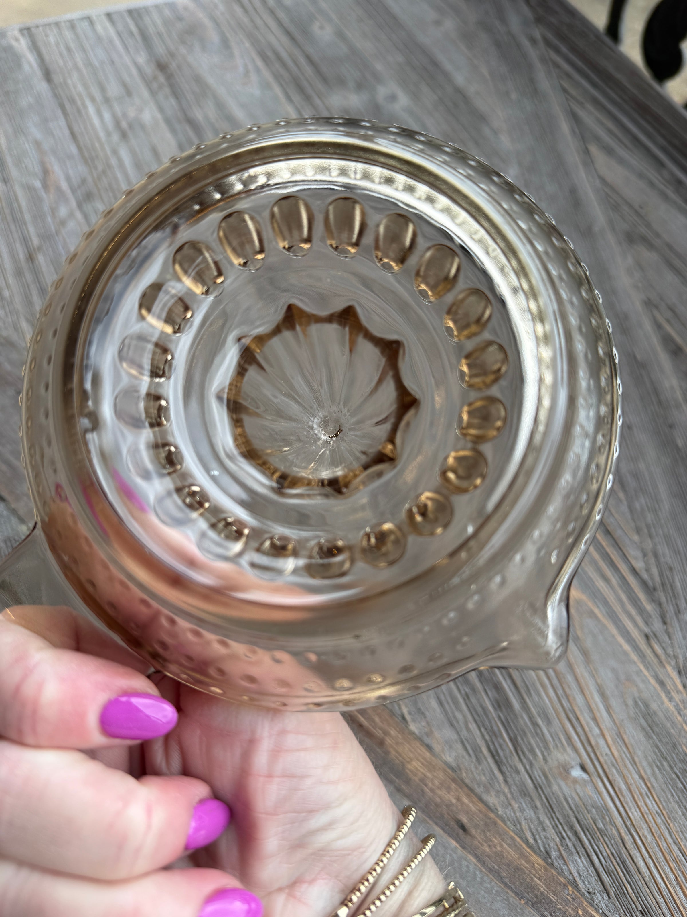 Close-up of a decorative glass item held by a hand with purple nail polish on a wooden surface.