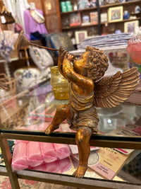 Gold cherub statue on a decorative stand with a blurred store interior in the background