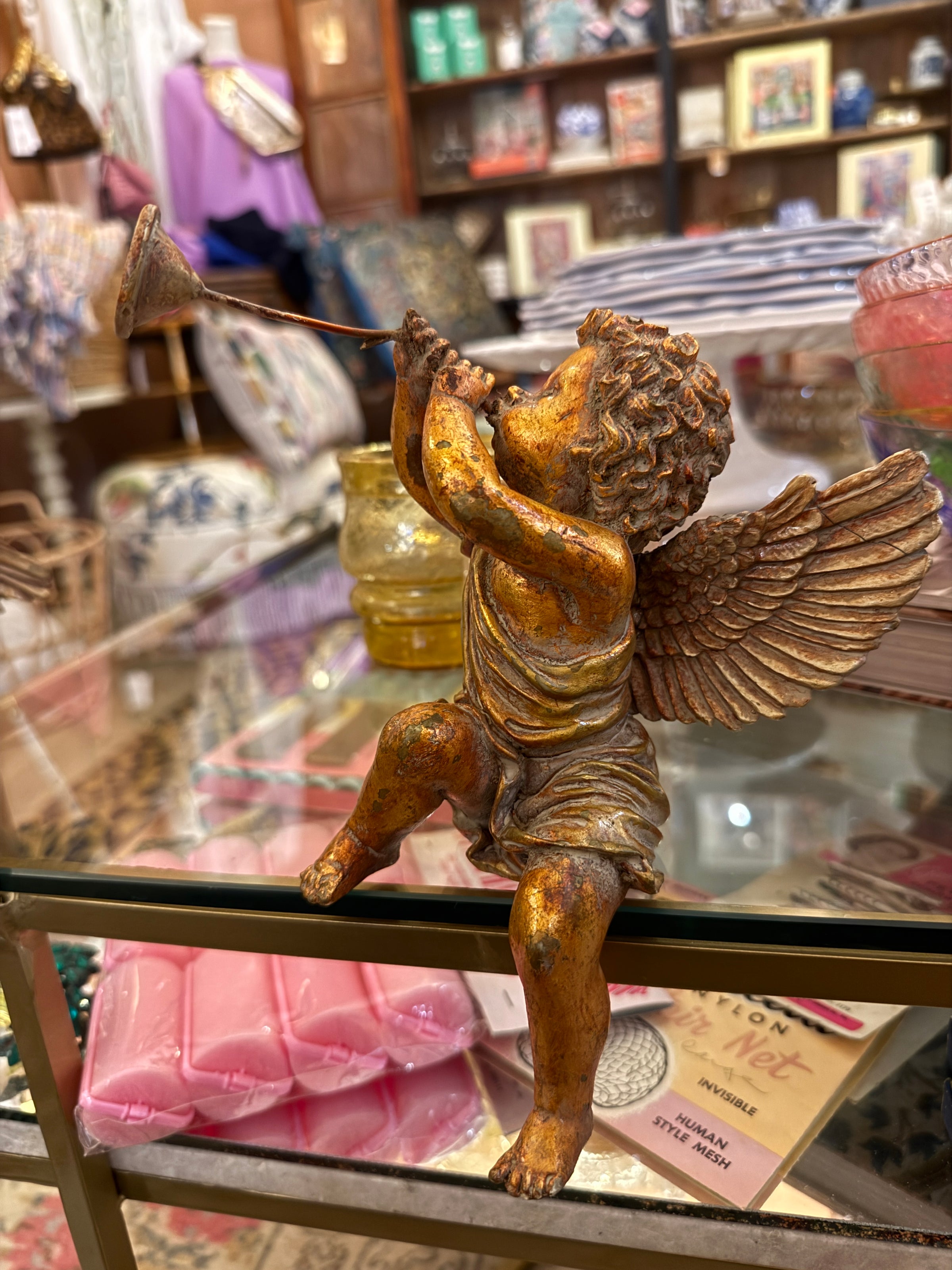 Gold cherub statue on a decorative stand with a blurred store interior in the background