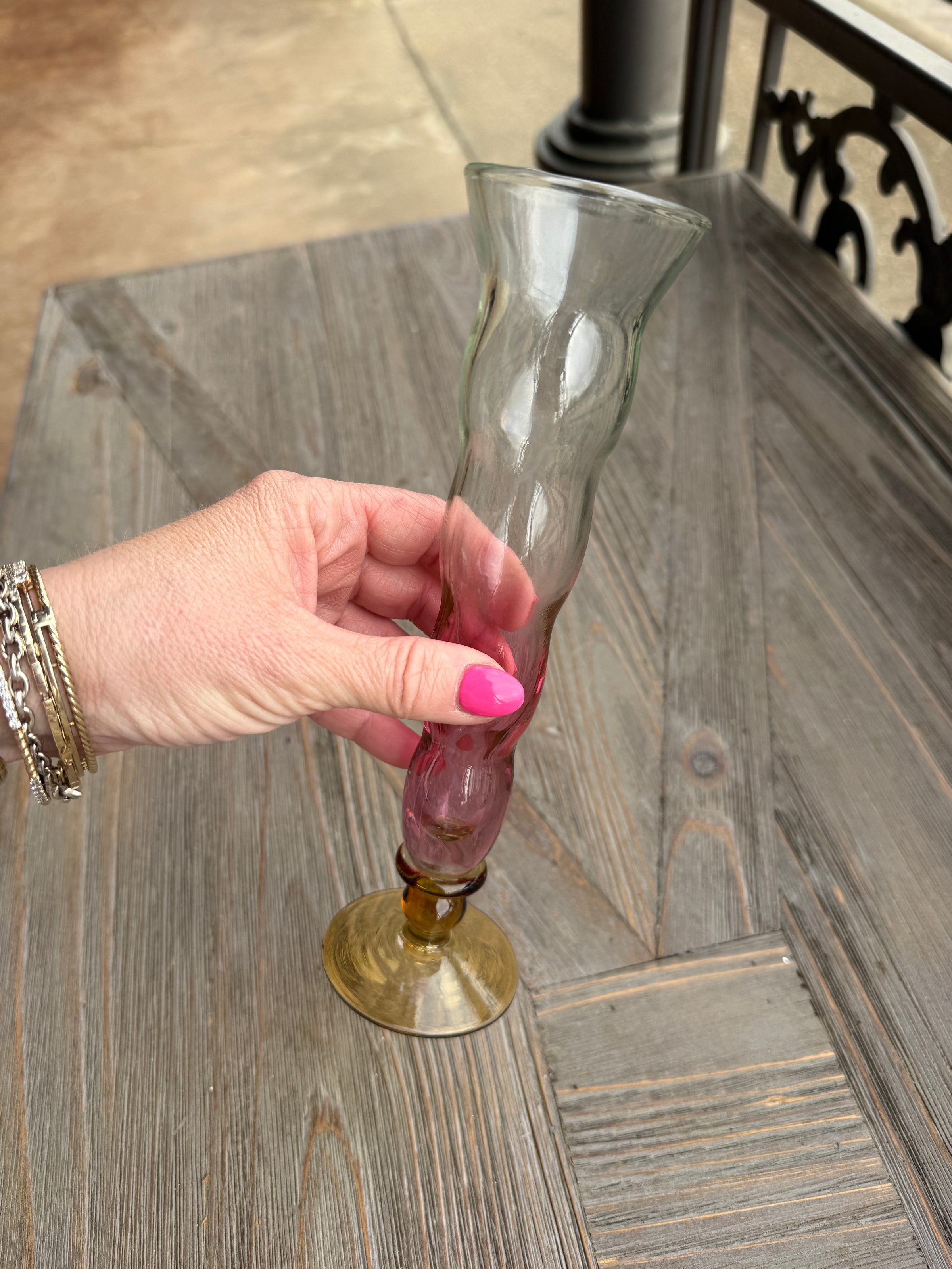 Hand with pink nail polish holding a glass bottle cap over a wooden surface