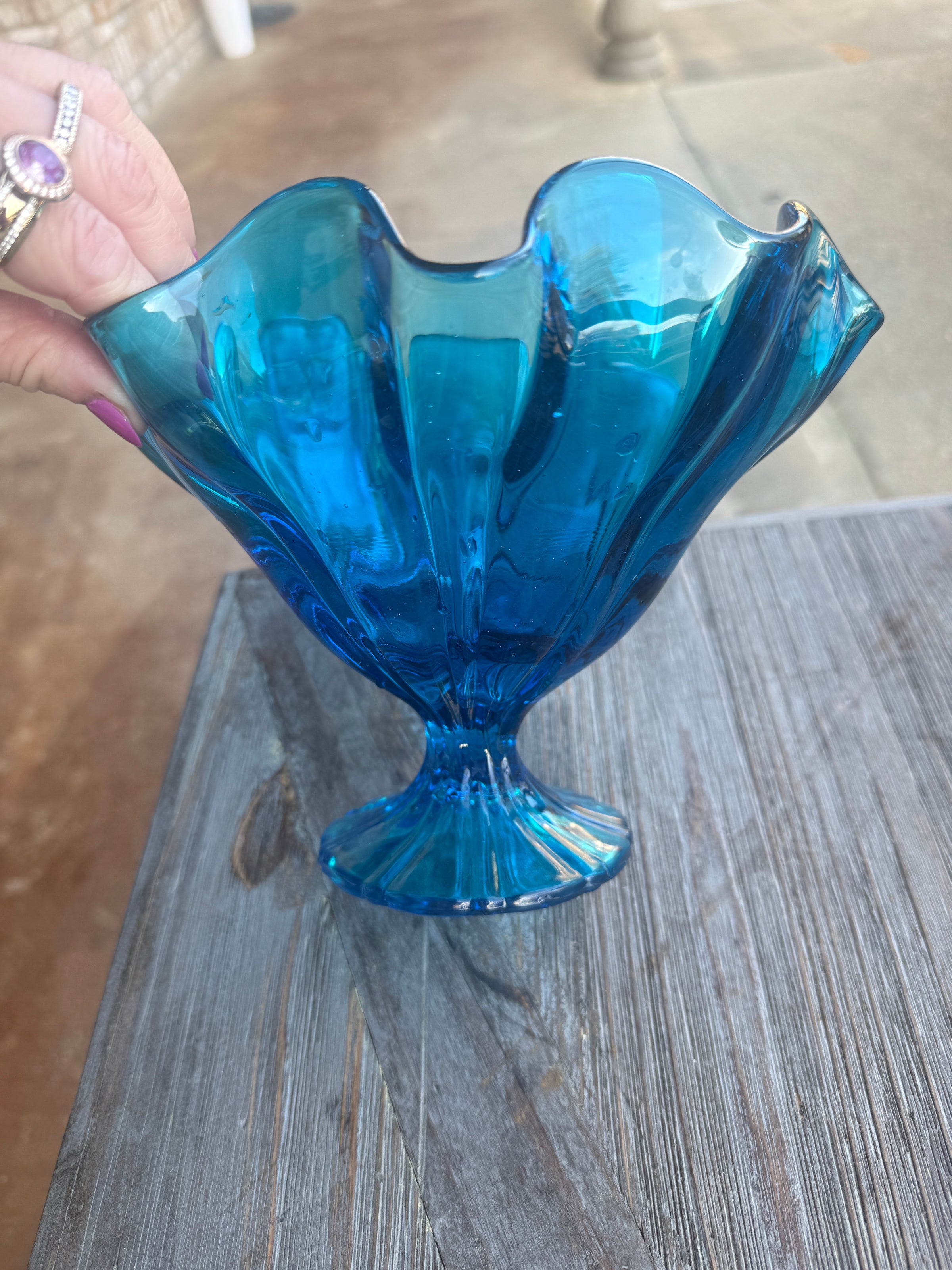 Blue glass fish ornament held against a wooden background