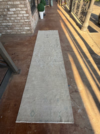A long, narrow beige area rug laid out on a concrete porch with brick walls and warm sunlight casting shadows.