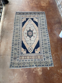 Vintage Turkish hand-knotted rug measuring approximately 3 feet 8 inches by 6 feet 4 inches with deep navy blue, cream, faded blush and green geometric medallion pattern.