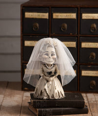Skeleton bride figurine with a veil on a wooden surface with vintage drawers in the background.