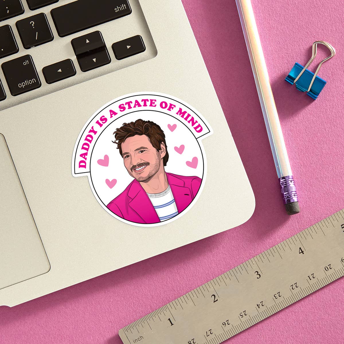 Sticker with a man's face and text 'Daddy is a State of Mind' on a laptop with stationery items.