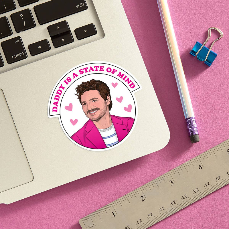 Sticker with a man's face and text 'Daddy is a State of Mind' on a laptop with stationery items.