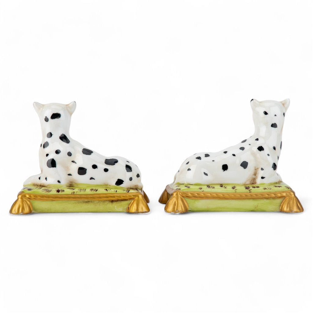 Two ceramic dalmatian dog figurines on green bases with gold accents against a white background.