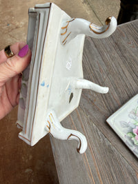 Decorative shelf with swan design held by a hand on a wooden surface