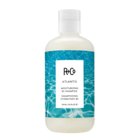A bottle of R+Co ATLANTIS Moisturizing Shampoo with a white and blue label design.