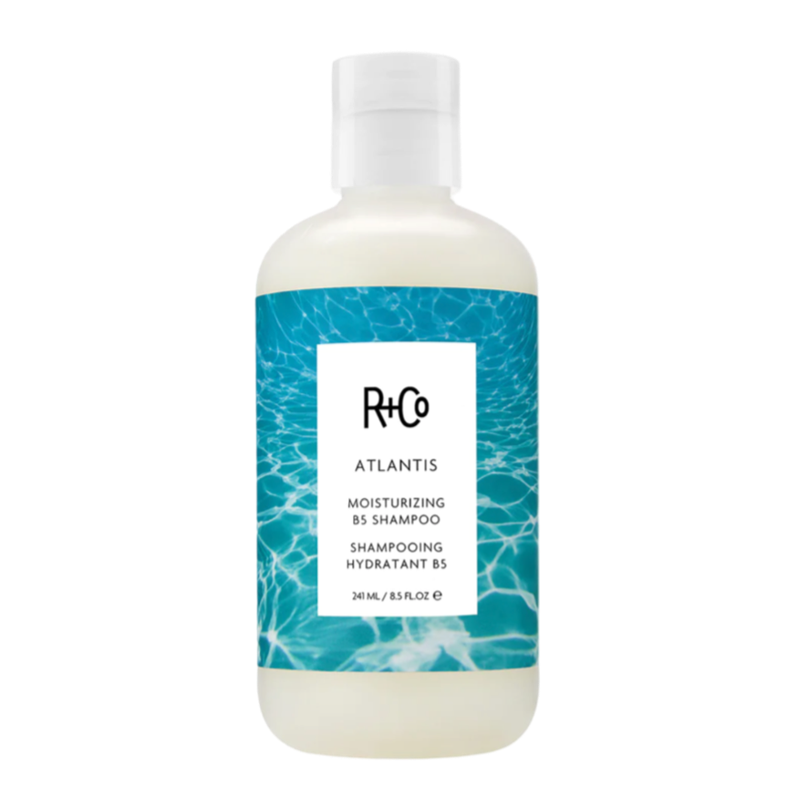 A bottle of R+Co ATLANTIS Moisturizing Shampoo with a white and blue label design.