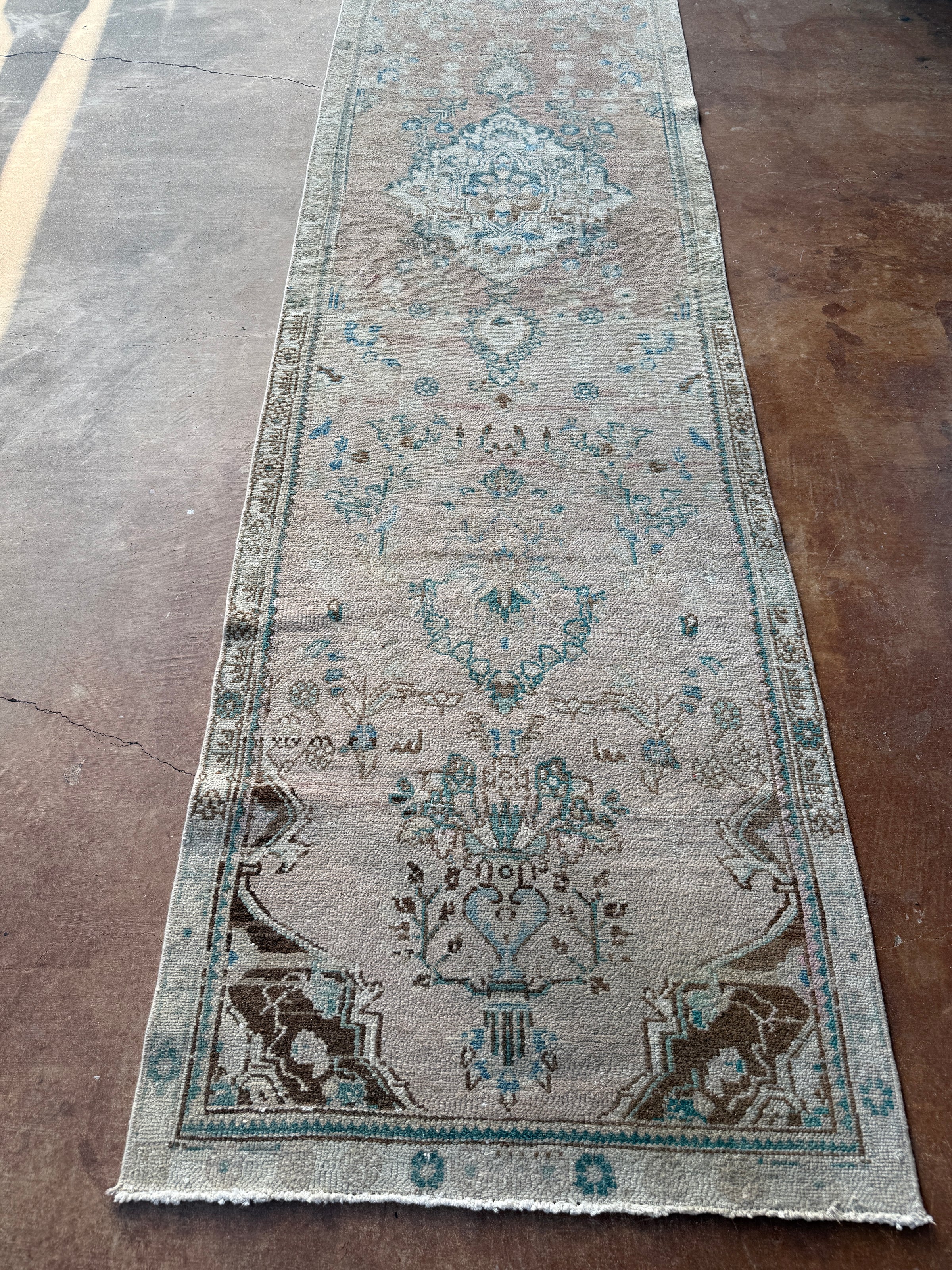 One-of-a-kind vintage Persian runner rug measuring approximately 2'11" x 12'5" with a faded dusty rose ground, blue and turquoise medallion motifs, ivory border and timeworn details.