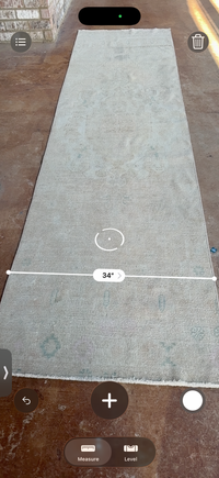 A long rectangular area rug laid flat on a brown floor, shown from above with a white measurement overlay indicating 34 inches in width.