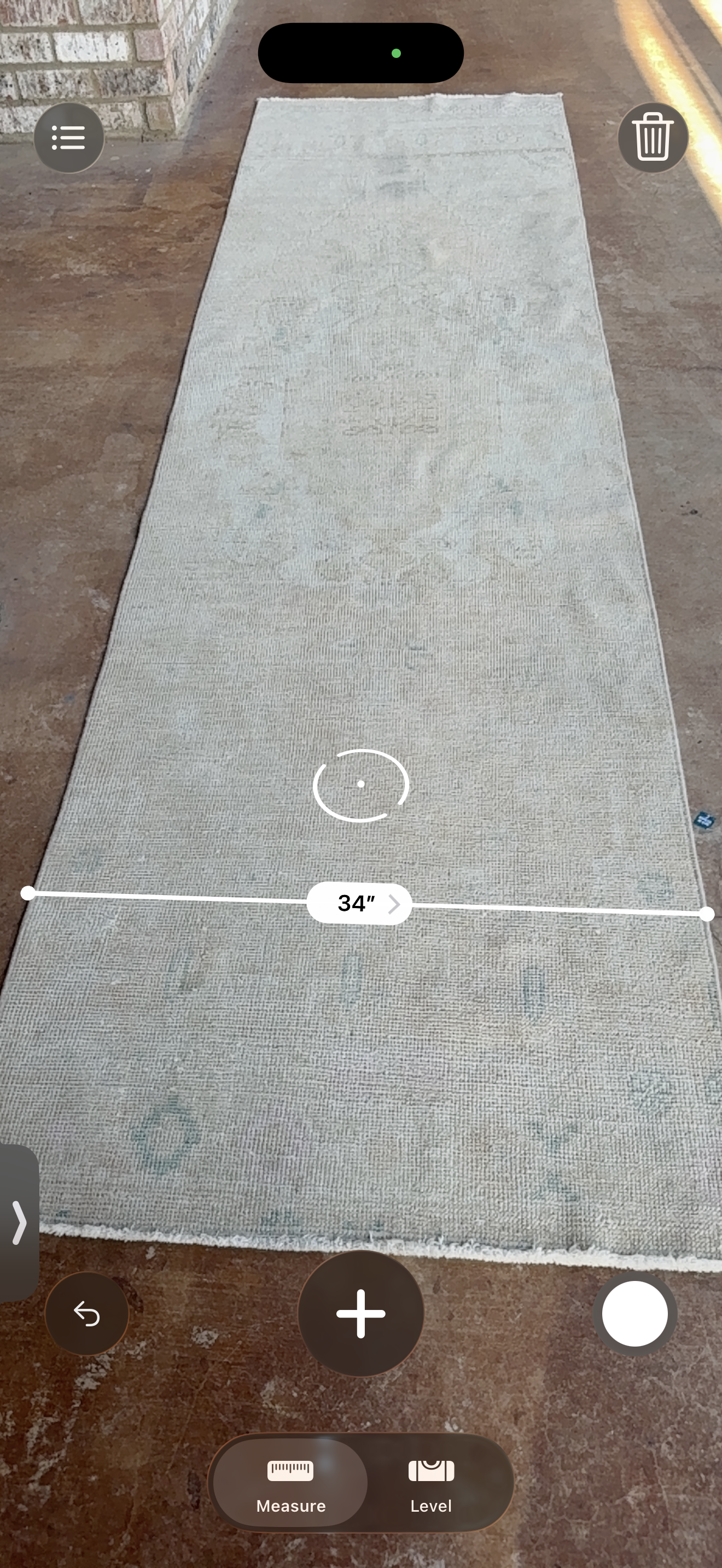 A long rectangular area rug laid flat on a brown floor, shown from above with a white measurement overlay indicating 34 inches in width.
