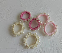 Set of pink and beige hair ties with pearl embellishments on a textured gray background