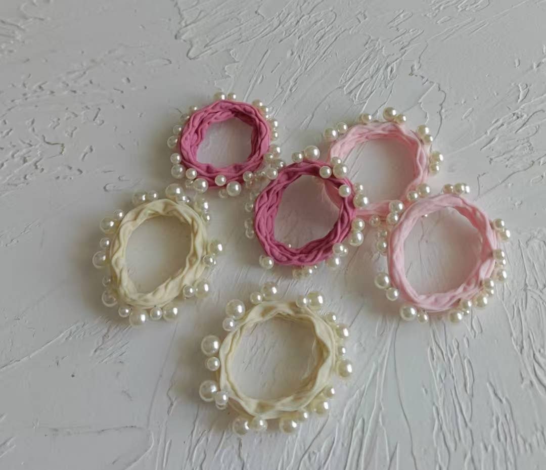 Set of pink and beige hair ties with pearl embellishments on a textured gray background