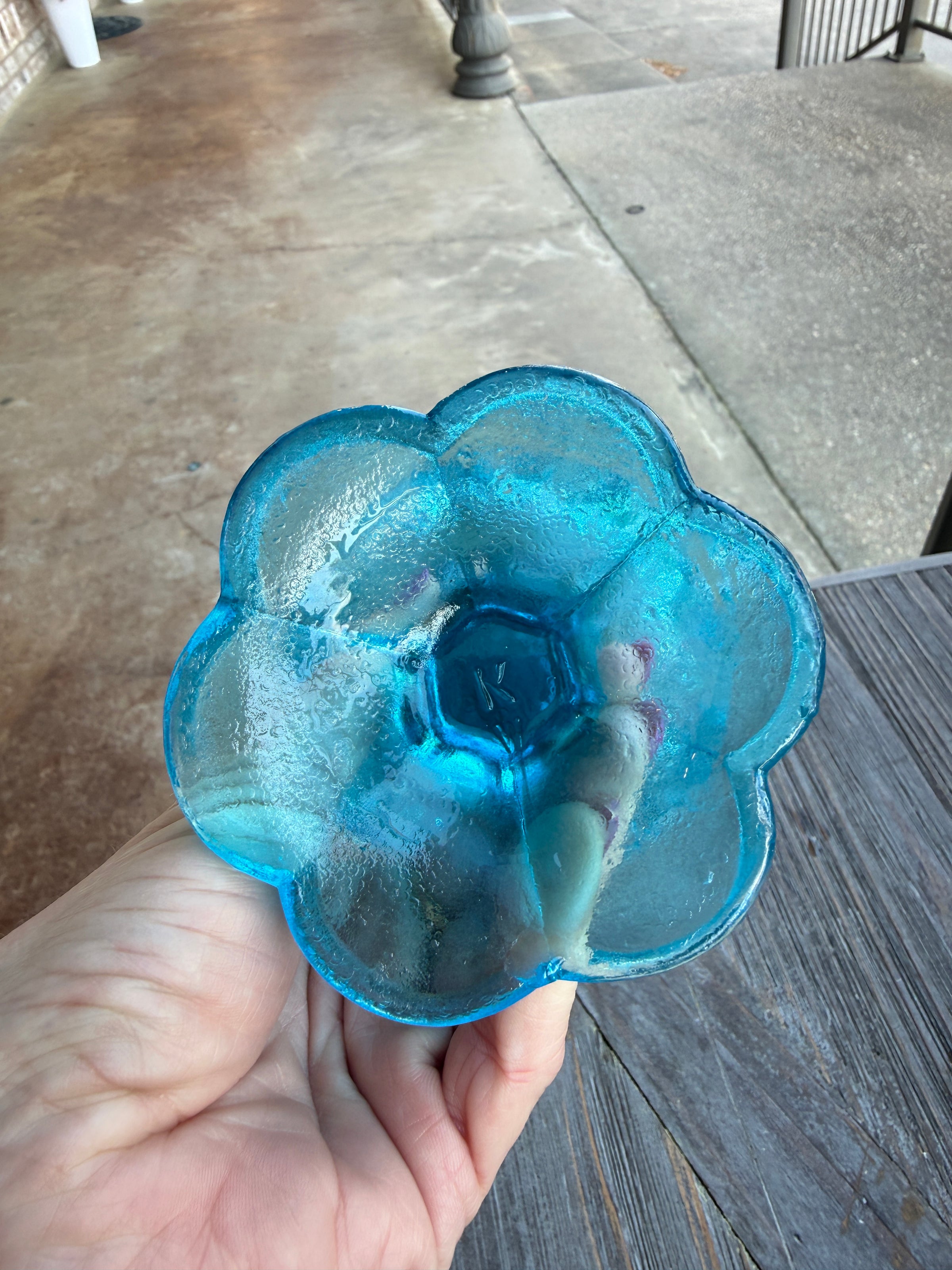 Blue glass flower held by a hand on a wooden surface
