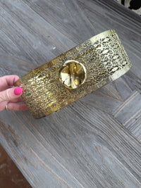 Gold clutch with intricate design held by a hand on a wooden surface