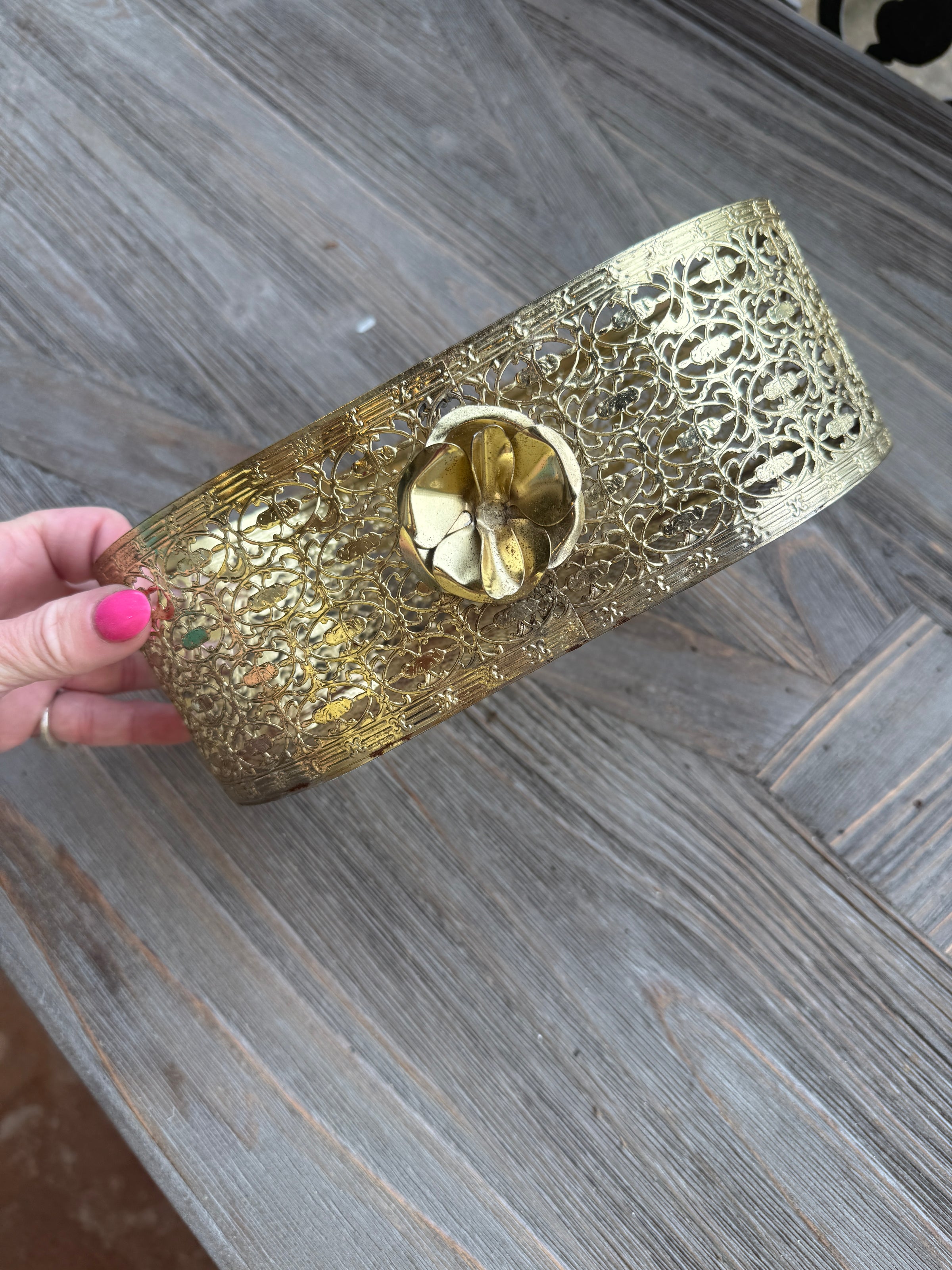 Gold clutch with intricate design held by a hand on a wooden surface