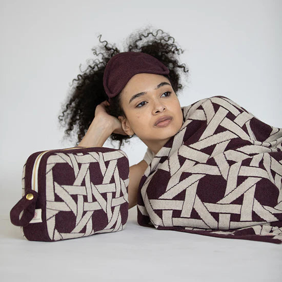 Woman wearing a patterned headband and blanket, holding a matching pouch against a white background