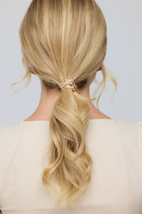 Blonde hair styled in a ponytail with a decorative clip against a neutral background