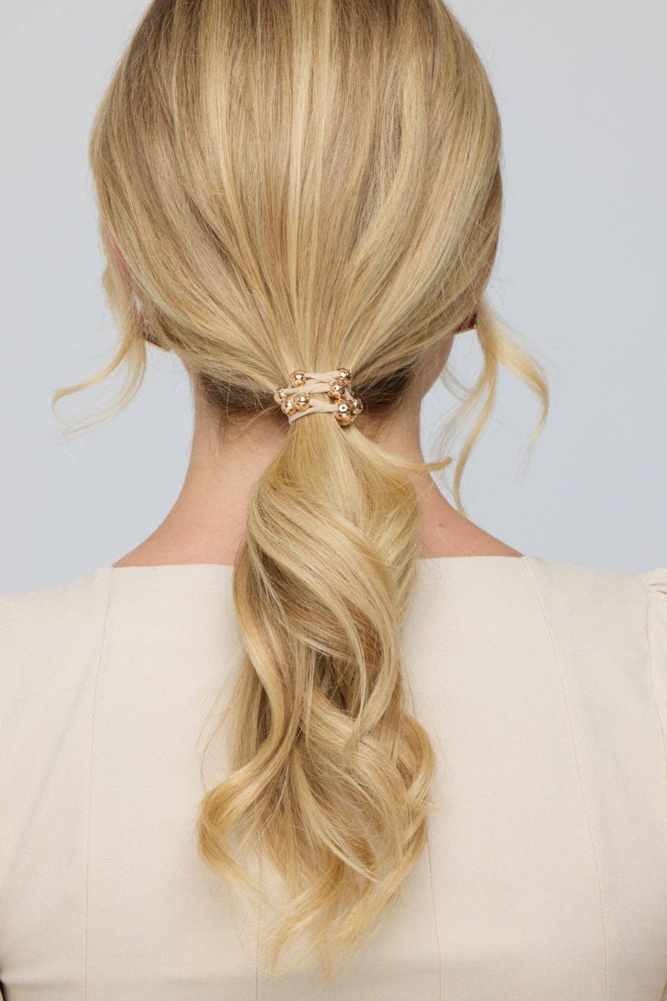 Blonde hair styled in a ponytail with a decorative clip against a neutral background