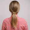 Person with blonde hair in a ponytail wearing a red and pink striped shirt on a plain background