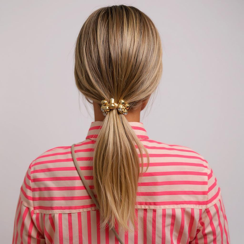 Person with blonde hair in a ponytail wearing a red and pink striped shirt on a plain background
