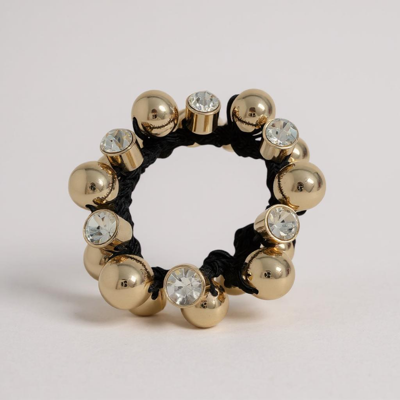 Gold beaded ring with black cord and clear crystals on a light gray background