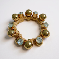 Bracelet with gold beads and crystal-like stones on a light pink background