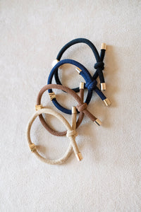 Three hair ties in navy, brown, and gold on a light beige background