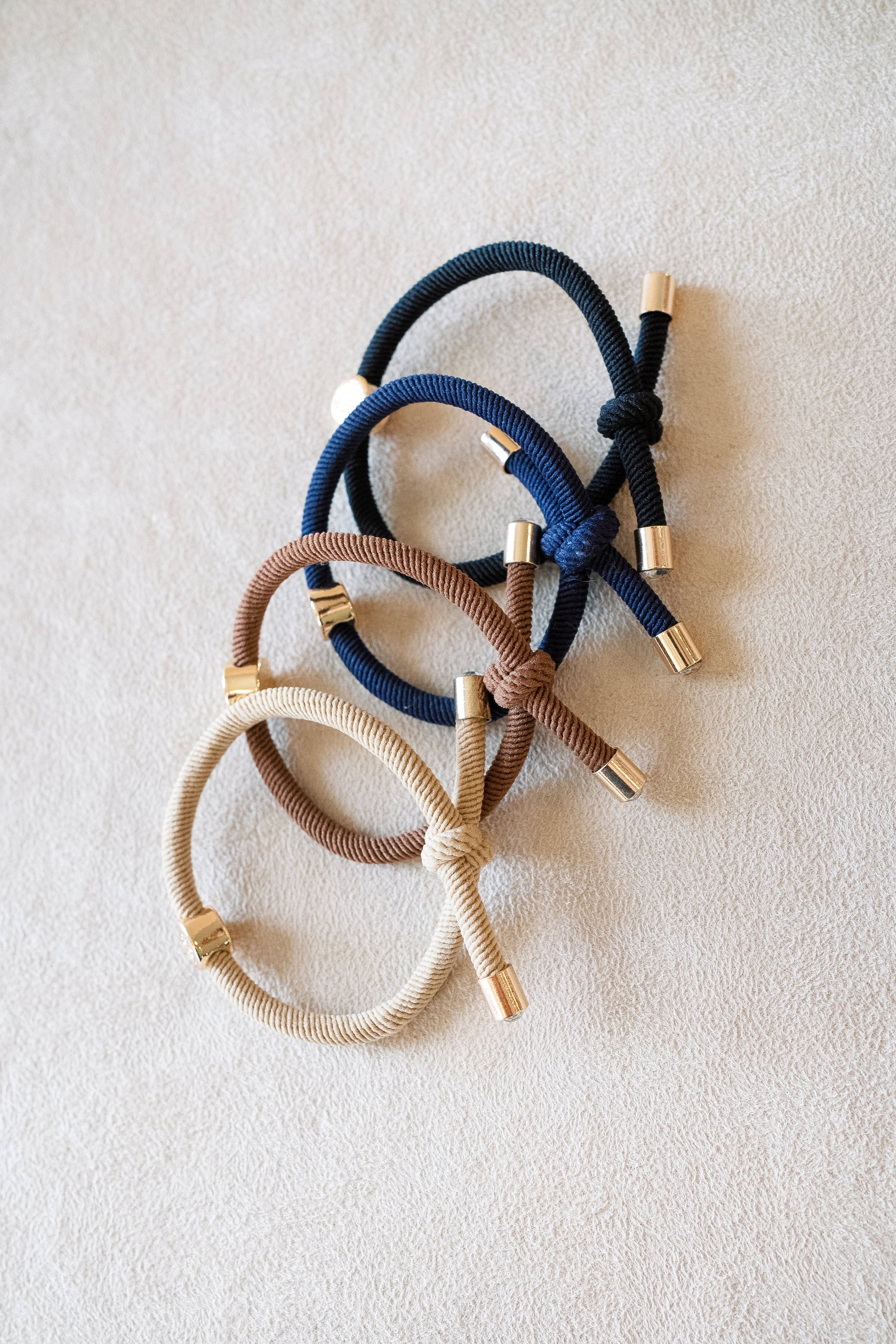 Three hair ties in navy, brown, and gold on a light beige background