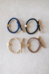 Four hair ties in blue, black, beige, and brown on a light gray background
