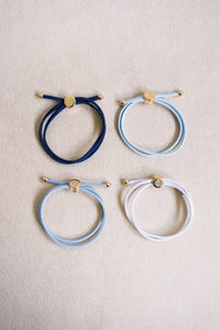 Four circular bracelets in blue, white, and gray on a beige background