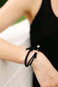 Black bracelet with gold accents on a wrist against a neutral background
