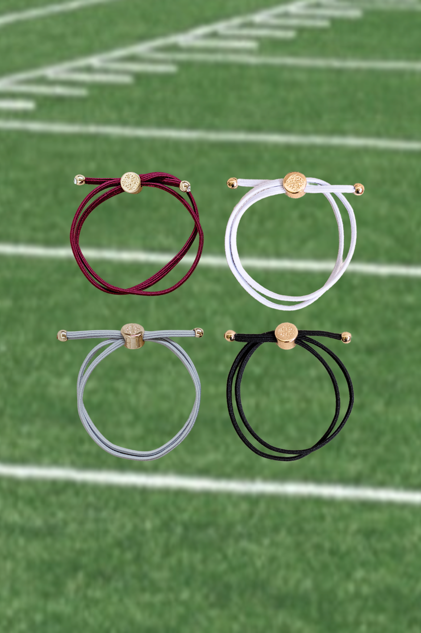 Four hair ties in red, white, gray, and black on a football field background
