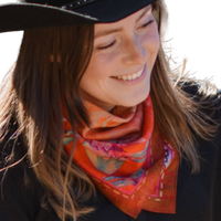 Woman wearing a colorful scarf and black hat, smiling outdoors.