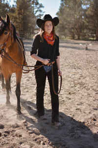 Woman in cowboy hat and scarf standing next to a horse in an outdoor setting