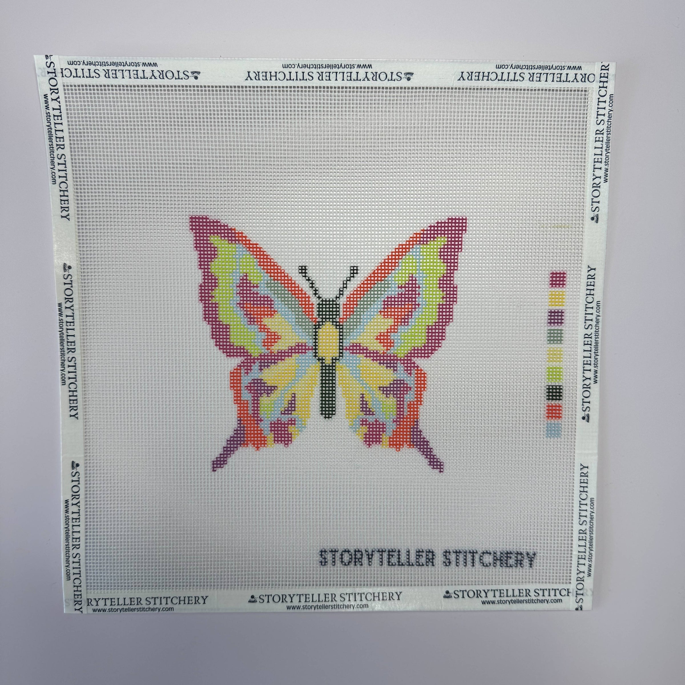 Cross-stitch pattern with a colorful butterfly design on a white background, branded 'Storyteller Stitchery'.