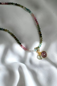 Necklace with multicolored beads and a pendant on a white fabric background