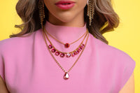 Close-up of a woman wearing a pink top and gold necklaces with red accents against a yellow background