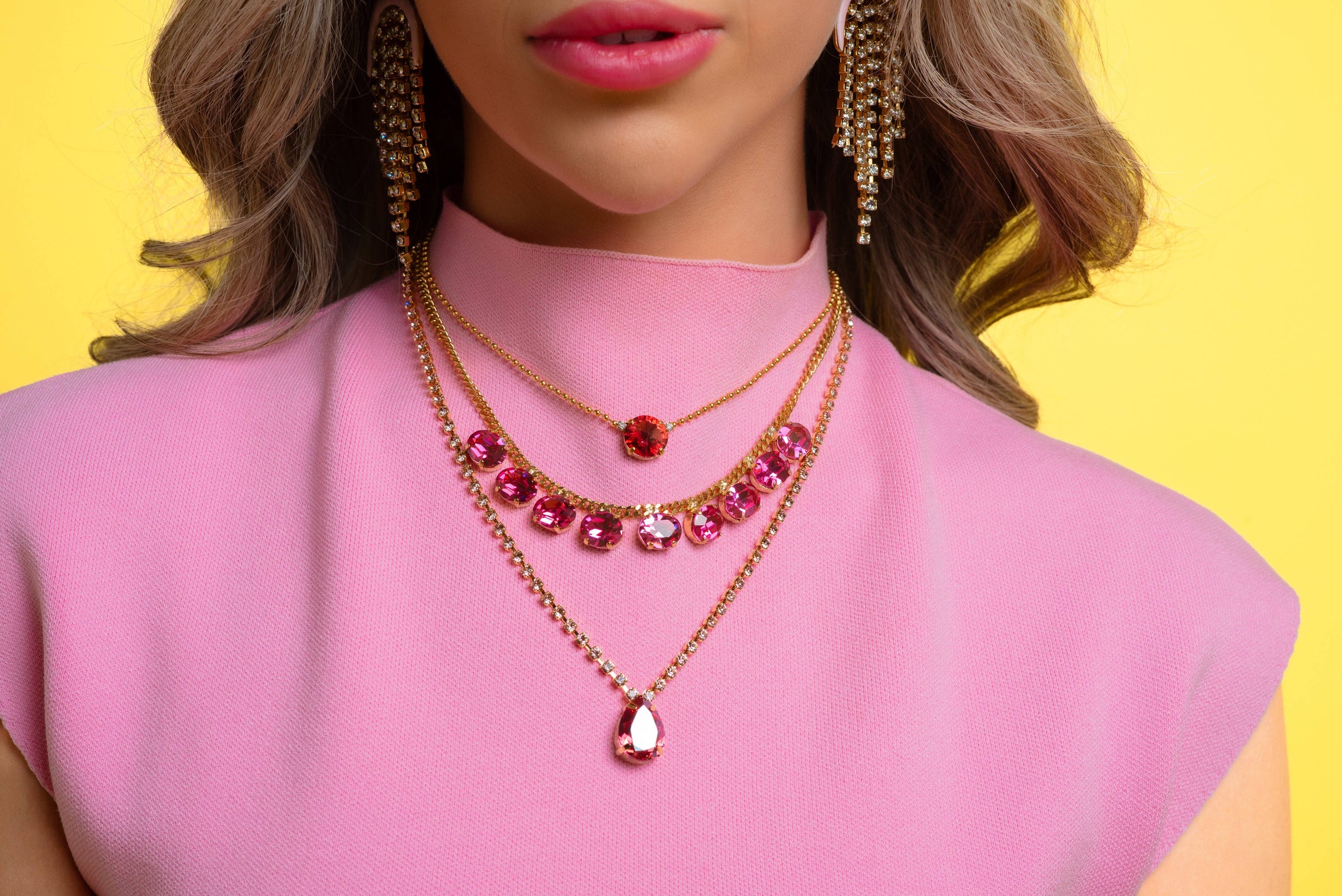 Close-up of a woman wearing a pink top and gold necklaces with red accents against a yellow background